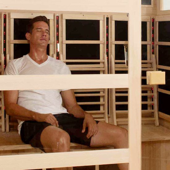 Man relaxing in a sauna, wearing a white shirt and black shorts, enjoying the heat therapy.