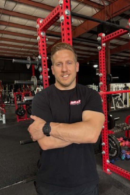Young man at gym wearing Beat Personal Training hoodie, standing in front of fitness equipment.