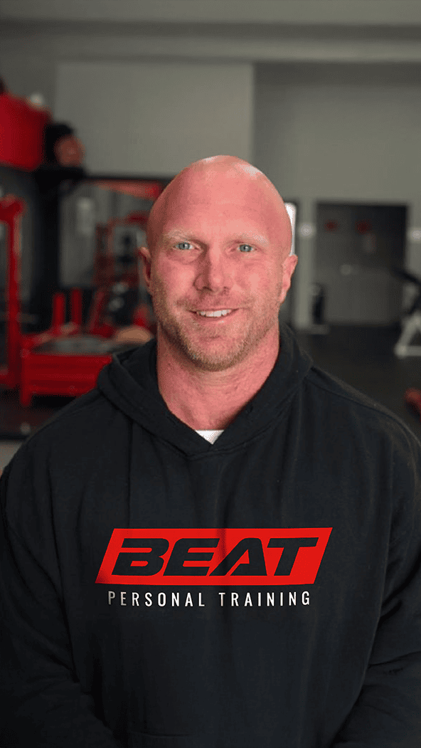 Trainer in gym wearing a Beat Personal Training hoodie, smiling confidently.