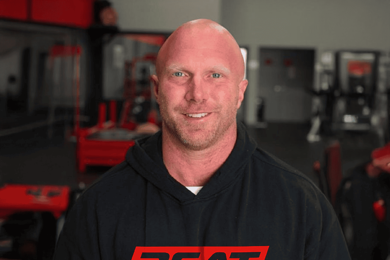 Bald man in a hoodie smiling in a gym setting.