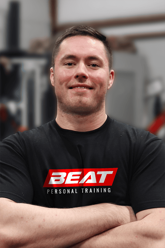 Man in Beat Personal Training shirt, smiling confidently in gym setting.