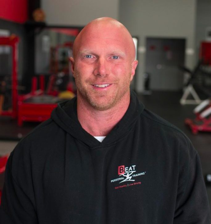 Man in gym hoodie smiling, inside a fitness training facility.