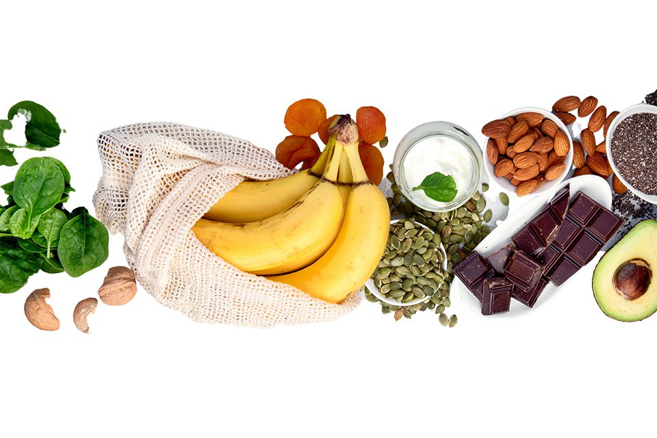 Healthy foods including bananas, spinach, almonds, and dark chocolate on white background.